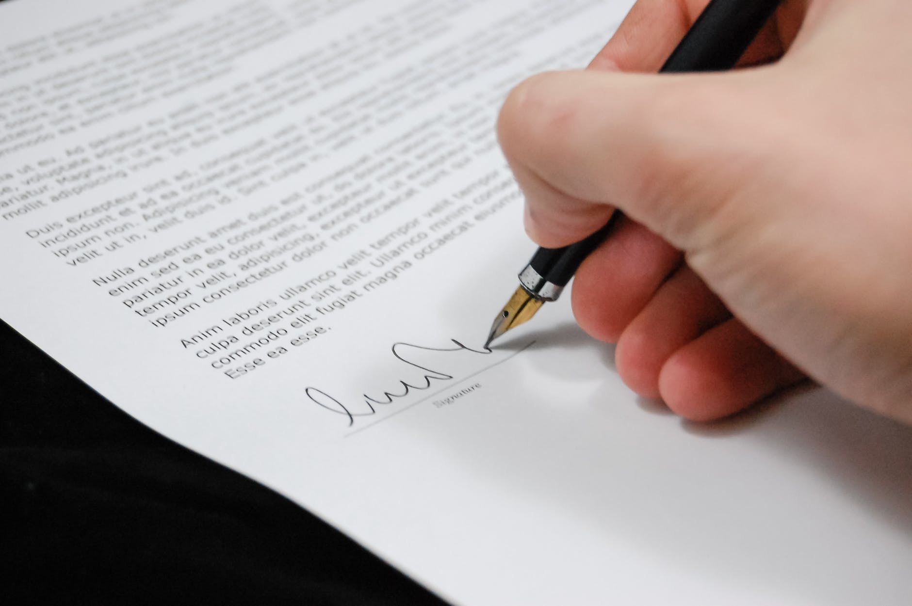 Close-up of a hand signing a form with a fountain pen, symbolizing secure client money protection.